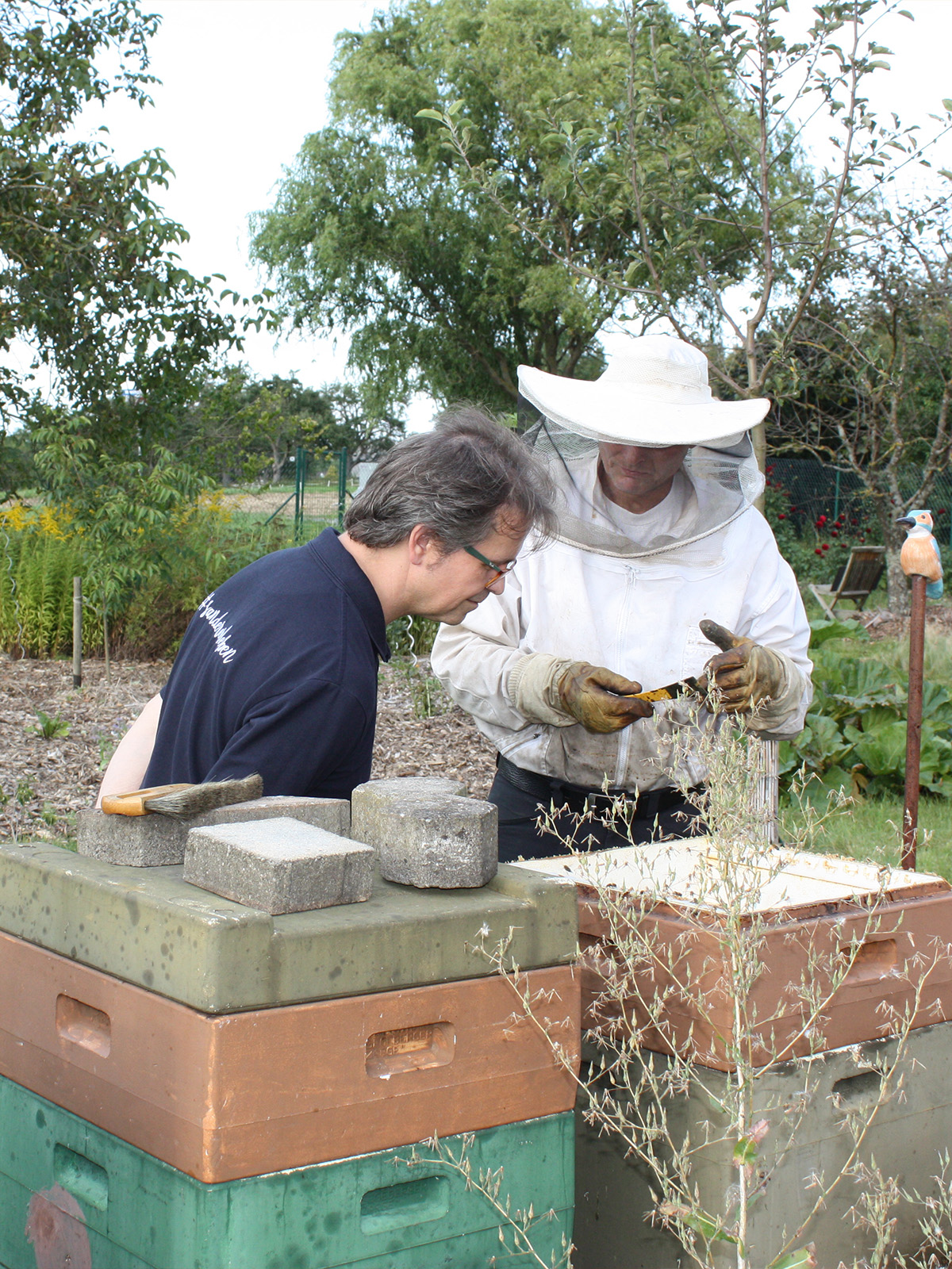 Director Stephan asks a beekeeper about bees. In the foreground, a beehive box.