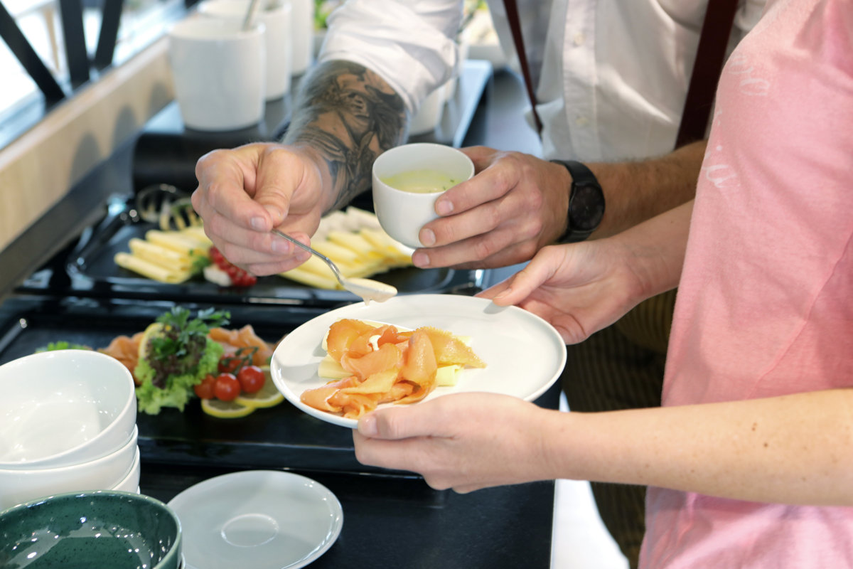 Zwei Personen am Frühstücksbüffet würzen ihren Lachs mit Sauce